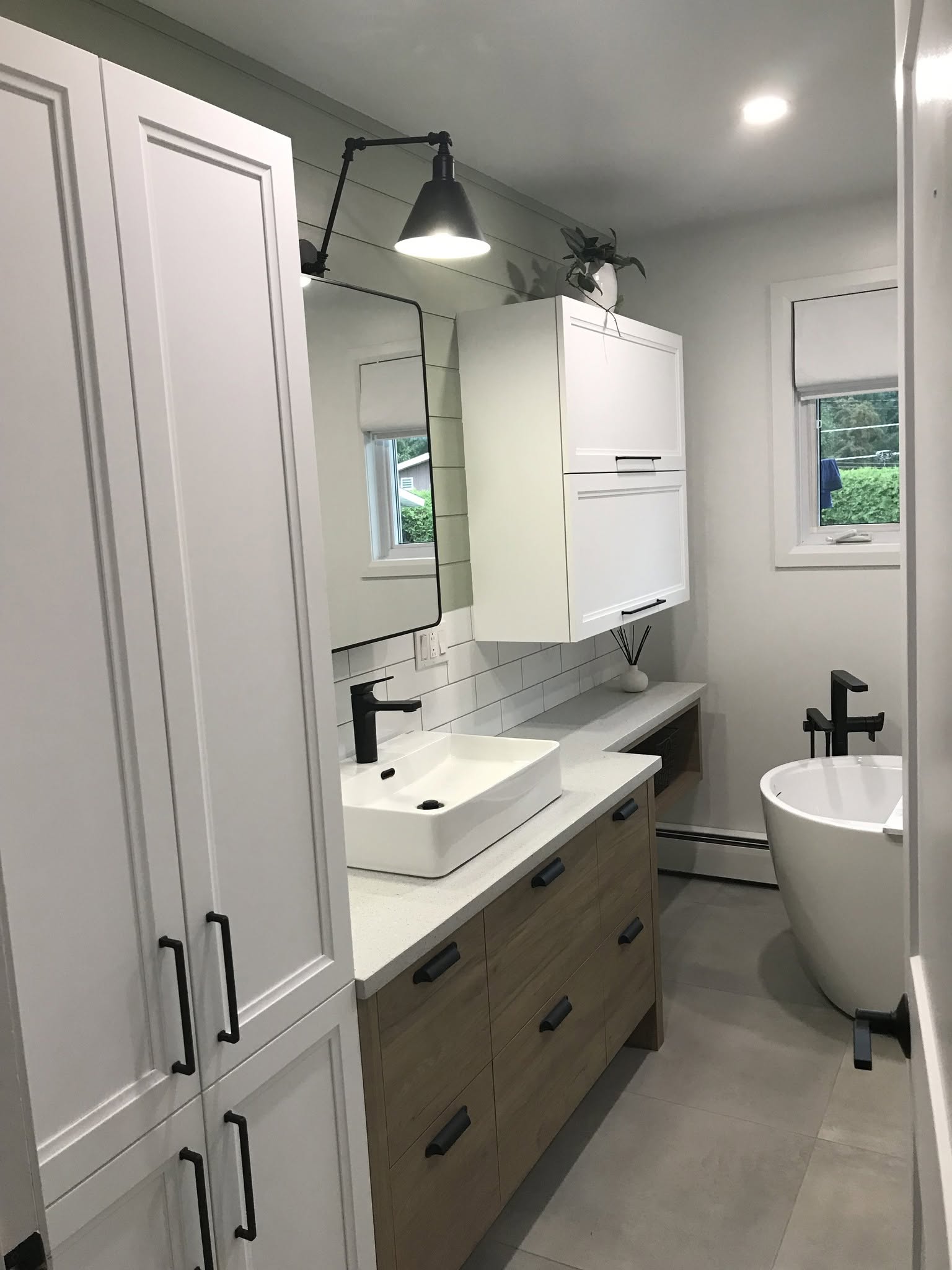 Salle de bain rénovée avec meuble-lavabo en bois, rangements blancs et robinetterie noire